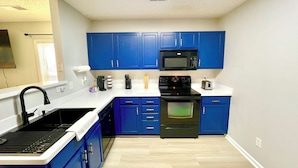 A kitchen with blue cabinets, a black microwave, a stove, and a sink.