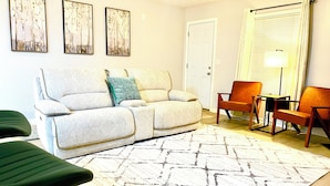 A living room with a sofa, two armchairs, a coffee table, and a patterned rug. There are three framed pictures on the wall.