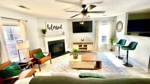 A modern living room with a fireplace, a ceiling fan, a flat-screen TV, and a dining area with bar stools.