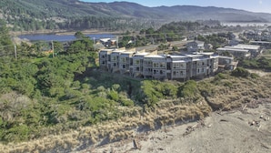 Un hotel de varios pisos con un diseño arquitectónico moderno, situado cerca de un lago y rodeado de colinas boscosas.
