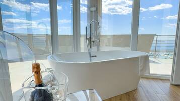 Un bagno moderno con una grande vasca da bagno, un box doccia in vetro e vista mare tramite ampie finestre.