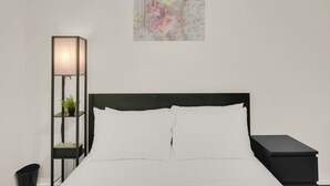 A neatly made bed with white linens, a black nightstand, a black floor lamp, and a wall-mounted painting of flowers. - Central Downtown 3BR with Workspaces Near NRG, Zoo, TSU & Medical Center (Houston)