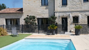 A stone building with a swimming pool, a lawn, and a black fence.