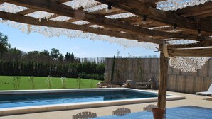 Een buitenzwembad met een pergola erboven, een tafel met stoelen en uitzicht op een gazon.