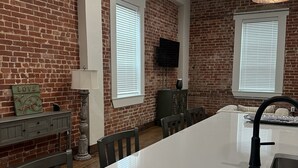 A modern kitchen with a large island, brick walls, and a flat-screen TV mounted above the island. - Cozy 2-bedroom apartment in Aubrey with WiFi, AC (Aubrey)