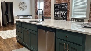 A modern kitchen with a large island, stainless steel dishwasher, and a motivational quote on the wall. - Cozy 2-bedroom apartment in Aubrey with WiFi, AC (Aubrey)