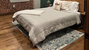A bedroom with a brick wall, a ceiling fan, a bed with a wooden headboard, and a patterned rug. - Cozy 2-bedroom apartment in Aubrey with WiFi, AC (Aubrey)