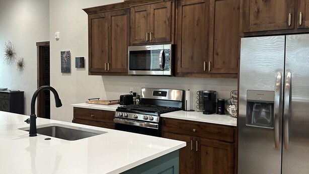 A modern kitchen with wooden cabinets, stainless steel appliances, and a central island with a sink. - Cozy 2-bedroom apartment in Aubrey with WiFi, AC (Aubrey)