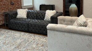 A living room with a brick wall, a dark grey sofa, a light grey armchair, and a large vase. - Cozy 2-bedroom apartment in Aubrey with WiFi, AC (Aubrey)
