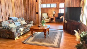 A cozy living room with a wooden floor, a patterned sofa, a coffee table, and a television. - Penthouse w/ Boho Loft, Jacuzzi, + Balcony -3 BR (Saint Joseph)