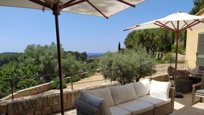 A terrace with a wicker sofa, dining table, and chairs, overlooking a scenic landscape with trees and a view of the sea. - Villa De luxe -air-conditioned-pool-14 persons, 7 bedrooms and 7 bathrooms, 11 beds (Sanary-sur-Mer)