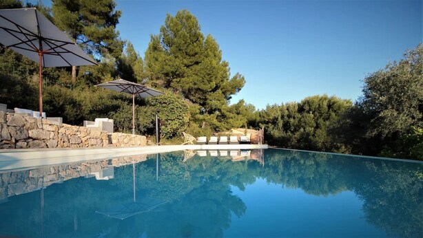 A clear swimming pool with a stone wall and lounge chairs, surrounded by trees and a clear sky. - Villa De luxe -air-conditioned-pool-14 persons, 7 bedrooms and 7 bathrooms, 11 beds (Sanary-sur-Mer)