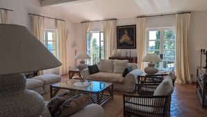 A spacious living room with a sofa set, a coffee table, and a wicker chair. There are two lamps on side tables, and a painting on the wall. - Villa De luxe -air-conditioned-pool-14 persons, 7 bedrooms and 7 bathrooms, 11 beds (Sanary-sur-Mer)