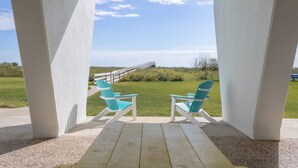 En inglasad veranda med två turkosa Adirondack-stolar som är placerade mot en gräsyta och ett trädäck.