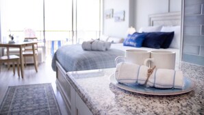 Ett modernt hotellrum med en stor säng, en matplats och en köksbänk med handdukar och muggar.