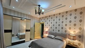 A bedroom with a large bed, a wardrobe, a mirror, and a nightstand with a lamp. - ZimaLeto (Yusufhona)