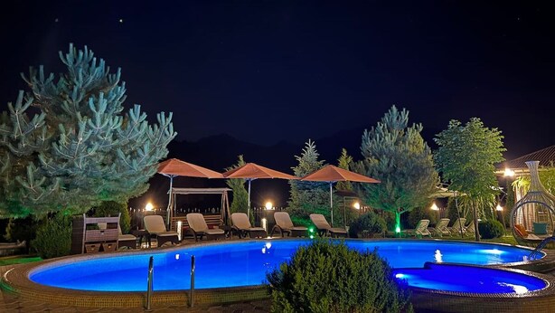 A nighttime swimming pool area with lounge chairs and umbrellas, surrounded by trees and a mountain backdrop. - ZimaLeto (Yusufhona)