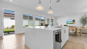 Cocina moderna con una isla grande, armarios blancos e iluminación colgante.