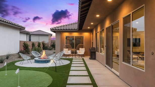 Un patio moderno con un brasero, mobiliario exterior y un césped cuidado.