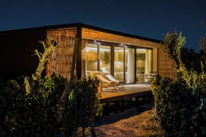 A modern, well-lit building with a glass facade, a wooden deck with lounge chairs, and a hanging light fixture. - Vibo Wine Lodge (Santa Cruz)