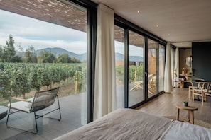 A modern bedroom with a large window, a bed, a small table, and a chair. - Vibo Wine Lodge (Santa Cruz)