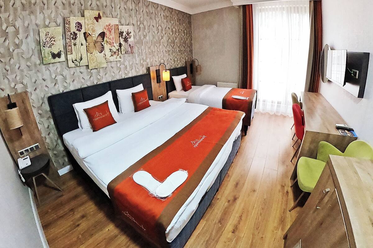 Une chambre d’hôtel avec deux lits, un bureau et une chaise. Elle est équipée de lampes murales et d’un téléviseur à écran plat.