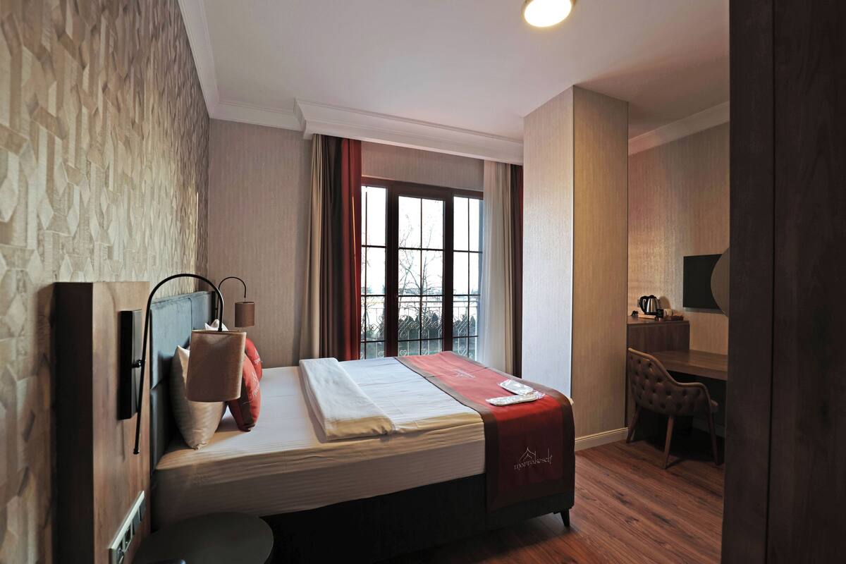Une chambre d’hôtel avec un lit, un bureau, une chaise et une fenêtre avec des rideaux.
