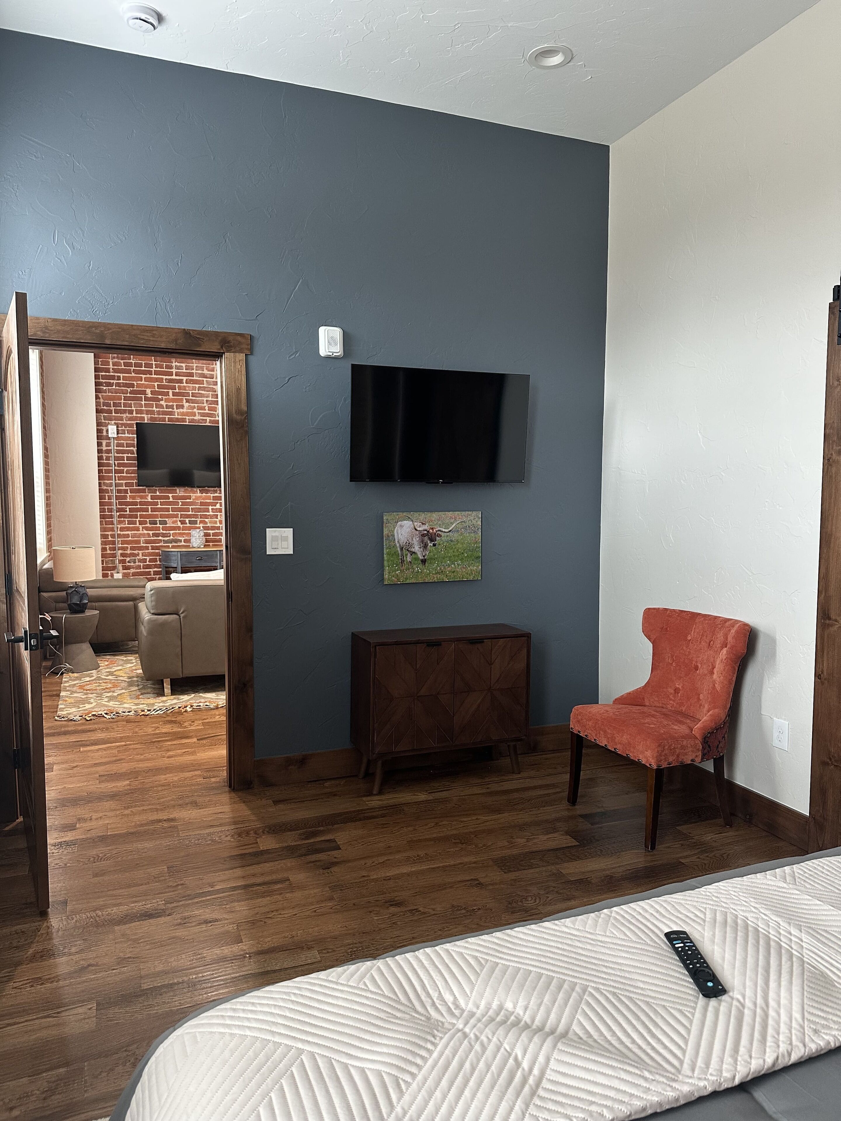 Una habitación con pared de ladrillo, un televisor montado, una silla roja y un armario de madera.