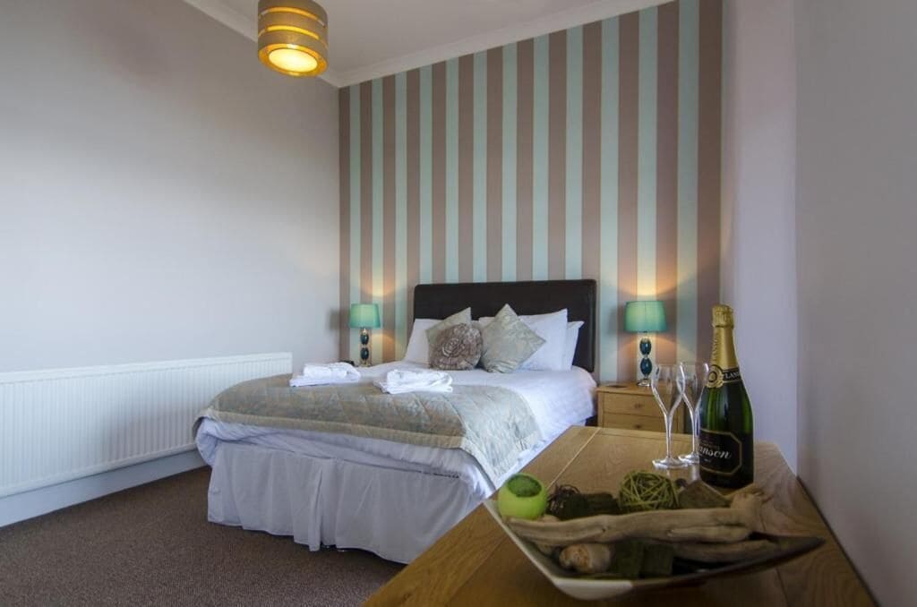 A hotel room with a bed, bedside lamps, a bottle of champagne, and a tray with fruits and nuts.