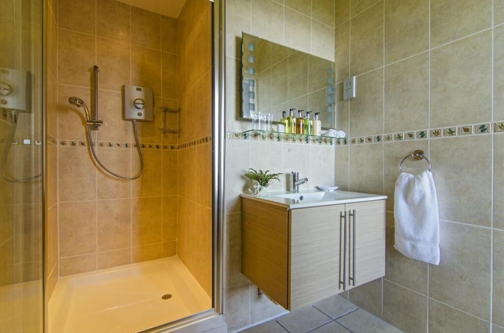 Un baño con ducha envuelta en vidrio, un lavabo con espejo y una toalla colgada en la pared.