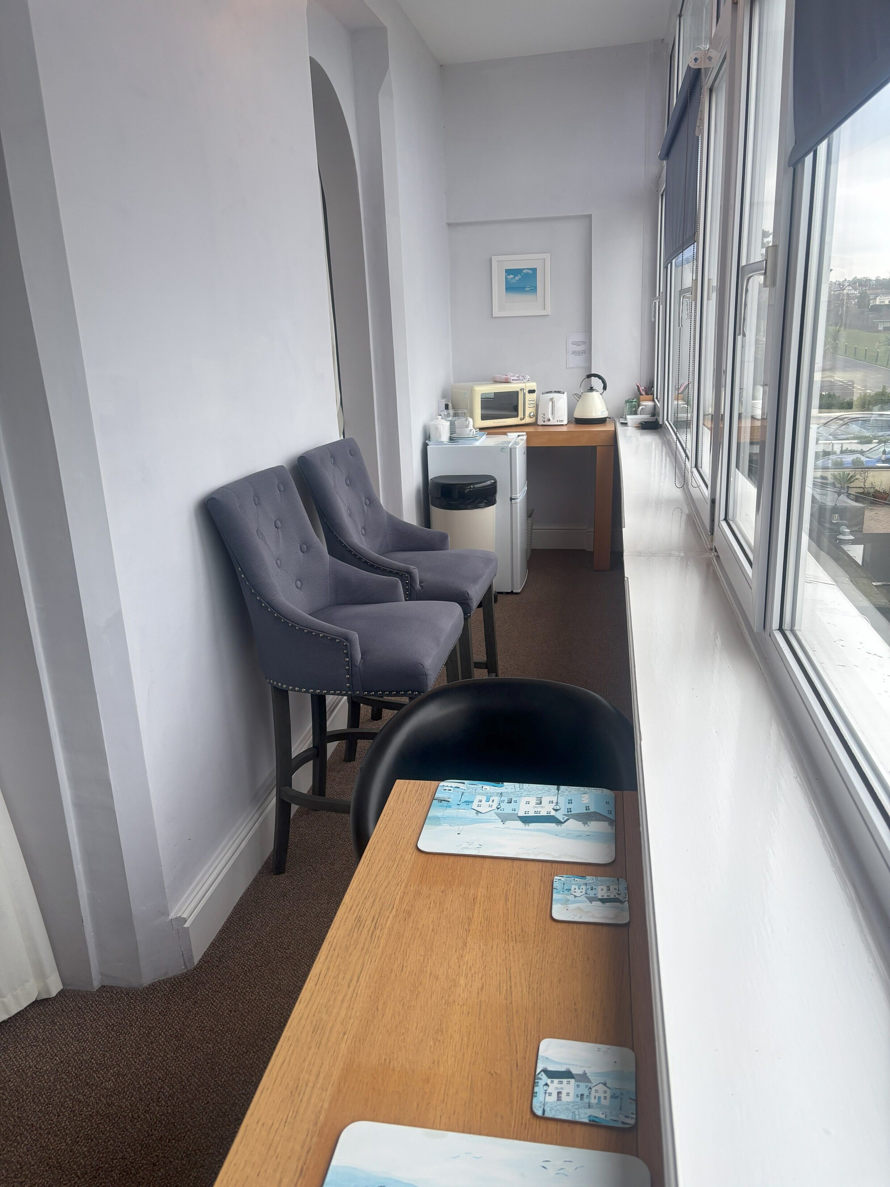 A small, modern room with a wooden desk, two grey chairs, a microwave, and a refrigerator.