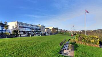 A grassy park area with a bench, a flagpole with flags, and a building with multiple stories and a blue sign.
