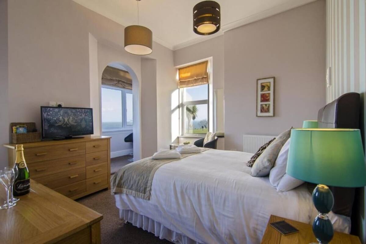Ein Schlafzimmer mit Bett, Nachttisch, Lampe, Fernseher und Blick ins Freie.