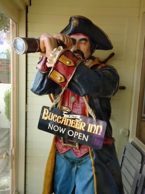 Una statua di un pirata che regge un cannocchiale, con un cartello che recita 'The Buccaneer Inn Now Open'.