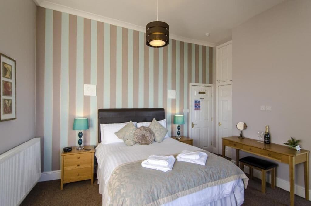 Une chambre à coucher bien rangée, avec un lit, des tables de chevet, un bureau et une porte.