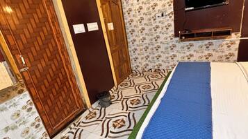 Un dormitorio con piso estampado, cama con cubrecama azul y blanco, puerta de madera y televisor montado en la pared.