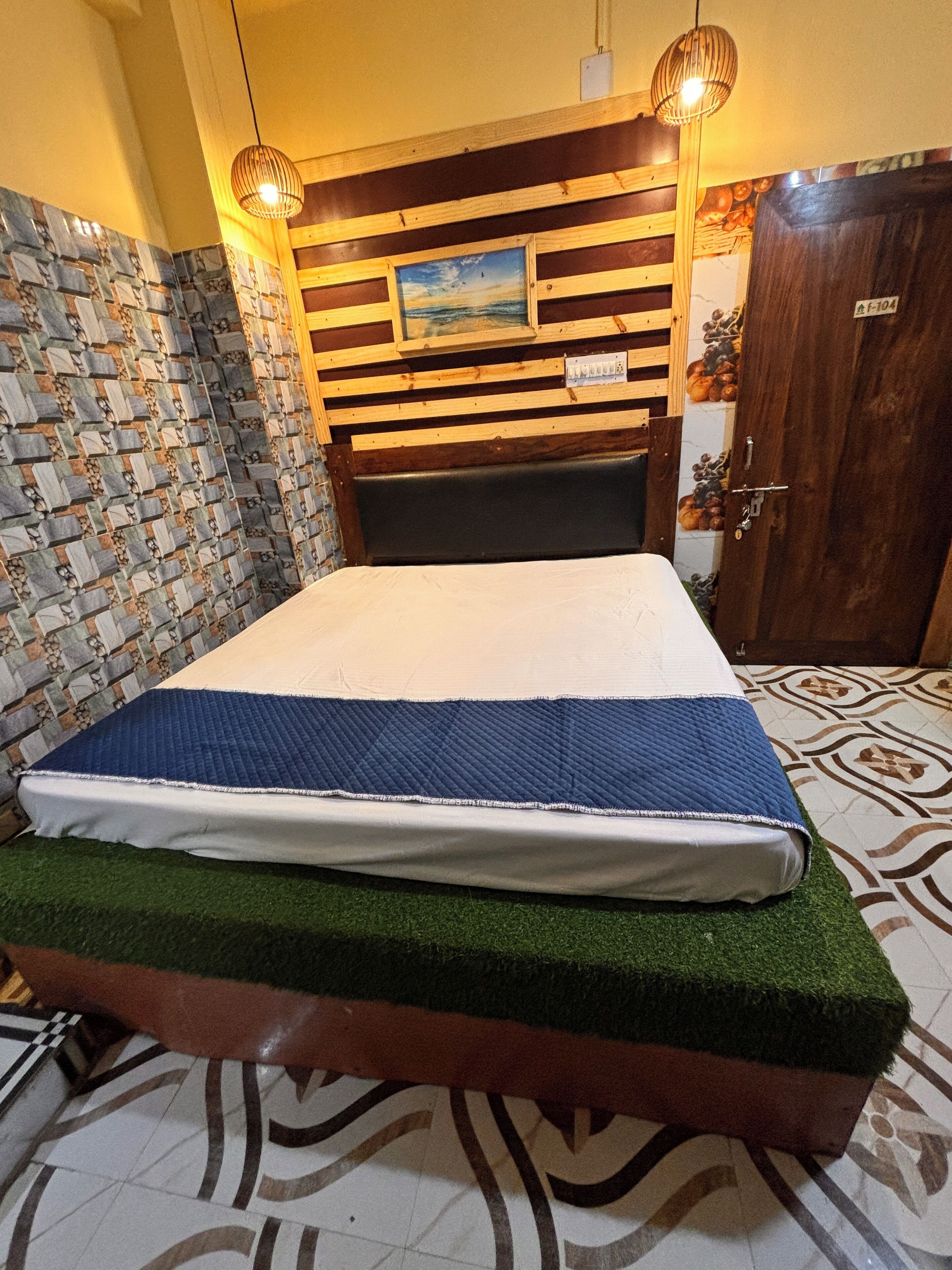 Ein Schlafzimmer mit einem Bett auf einer Plattform aus grünem Kunstgrün, einem Holz-Kopfteil mit einem Gemälde und einer Wand mit Muster.