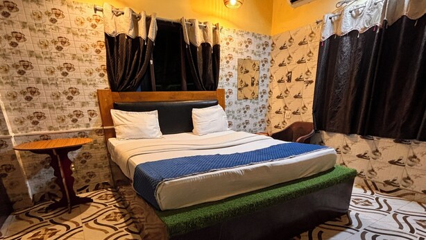 A bedroom with a bed, a small table, patterned wallpaper, and a tiled floor. - Plush hotels (Bhubaneshwar)
