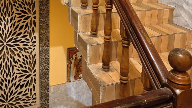 Eine Holztreppe mit Geländer, die zu einer Zwischenebene mit dekorativer Verkleidung und einer Wand mit floralen Kacheln führt.