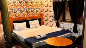 A hotel room with a bed, a round wooden table, a patterned floor, and a floral wallpaper. - Plush hotels (Bhubaneshwar)