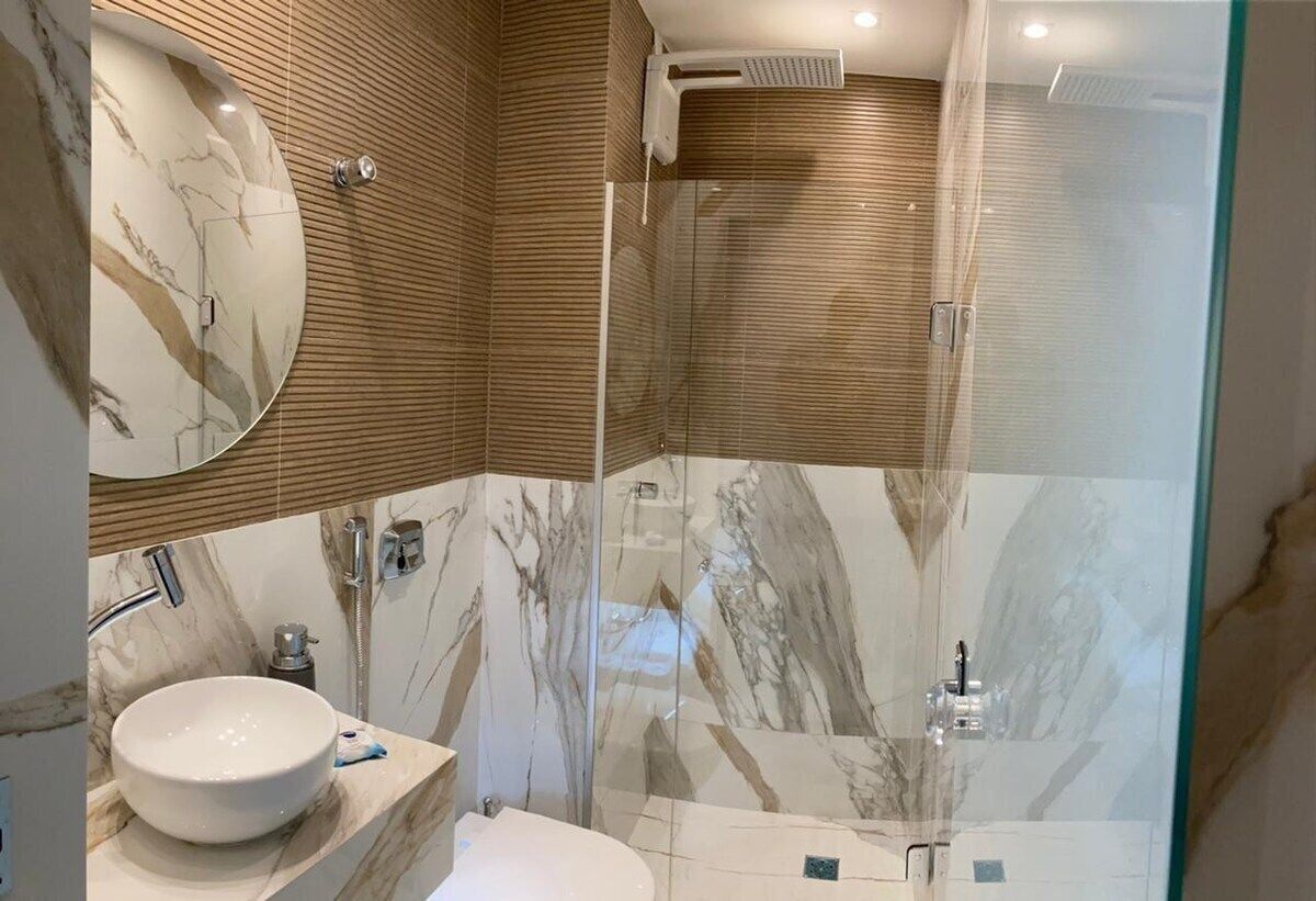 Un baño moderno con lavamanos de mármol, ducha con cerramiento de vidrio y paneles de madera en las paredes.