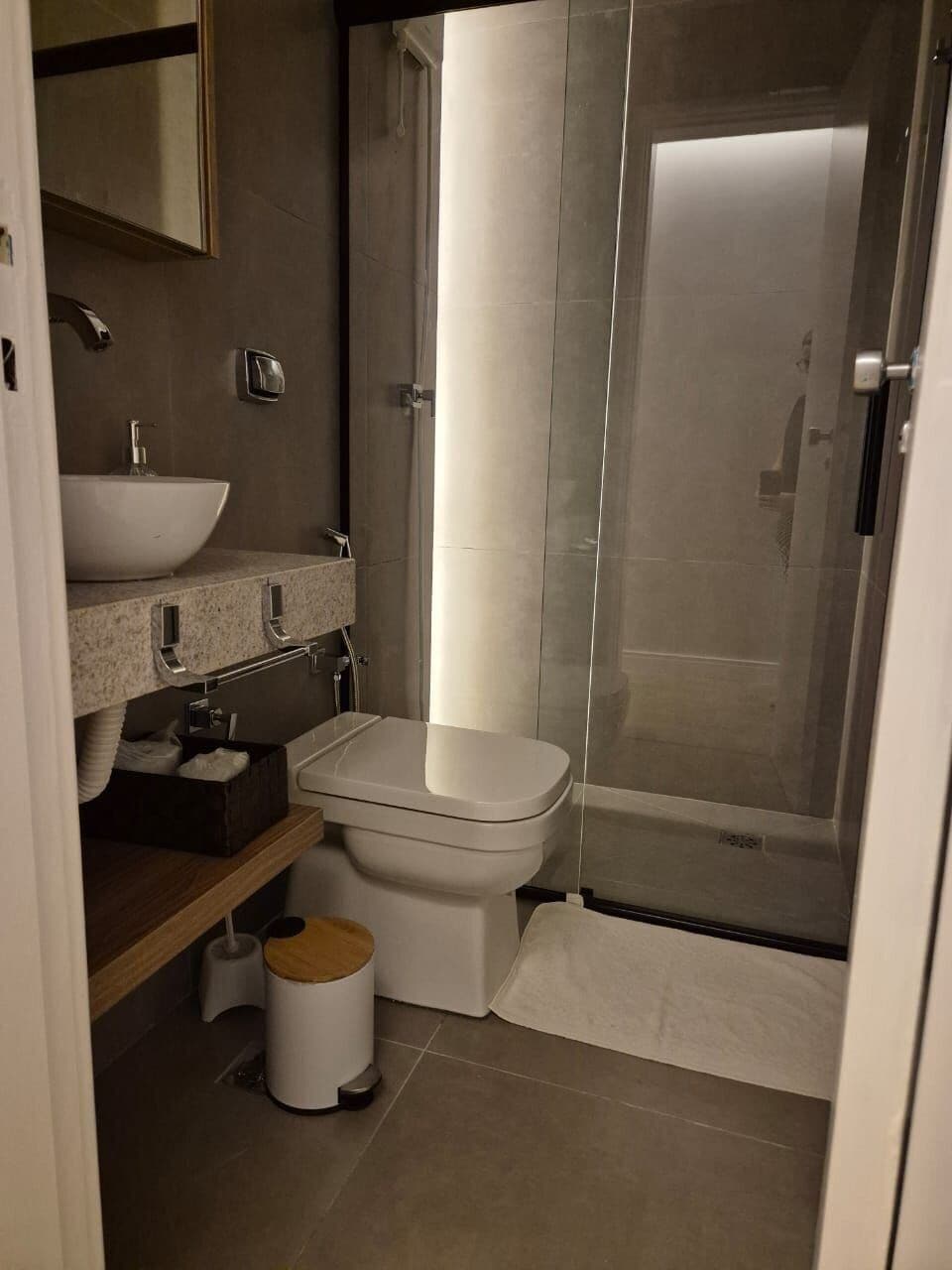 Un baño moderno con cabina de ducha de vidrio, inodoro blanco y lavamanos con encimera de mármol.