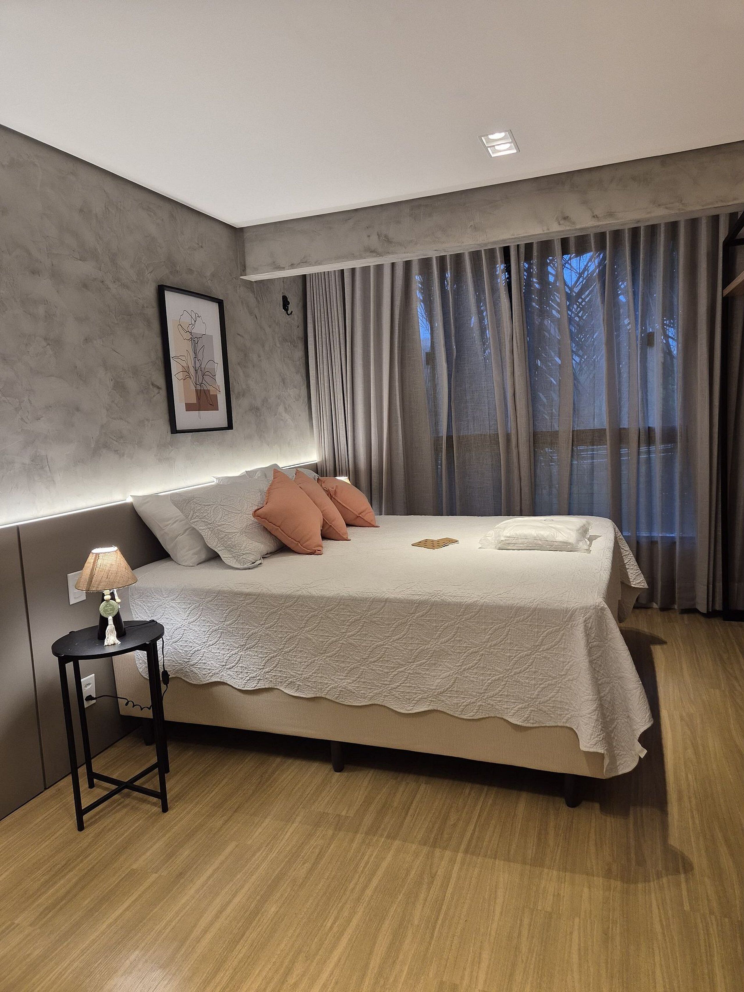 Ein modernes Schlafzimmer mit einem großen Bett, einem Nachttisch mit Lampe und einem gerahmten Bild an der Wand.