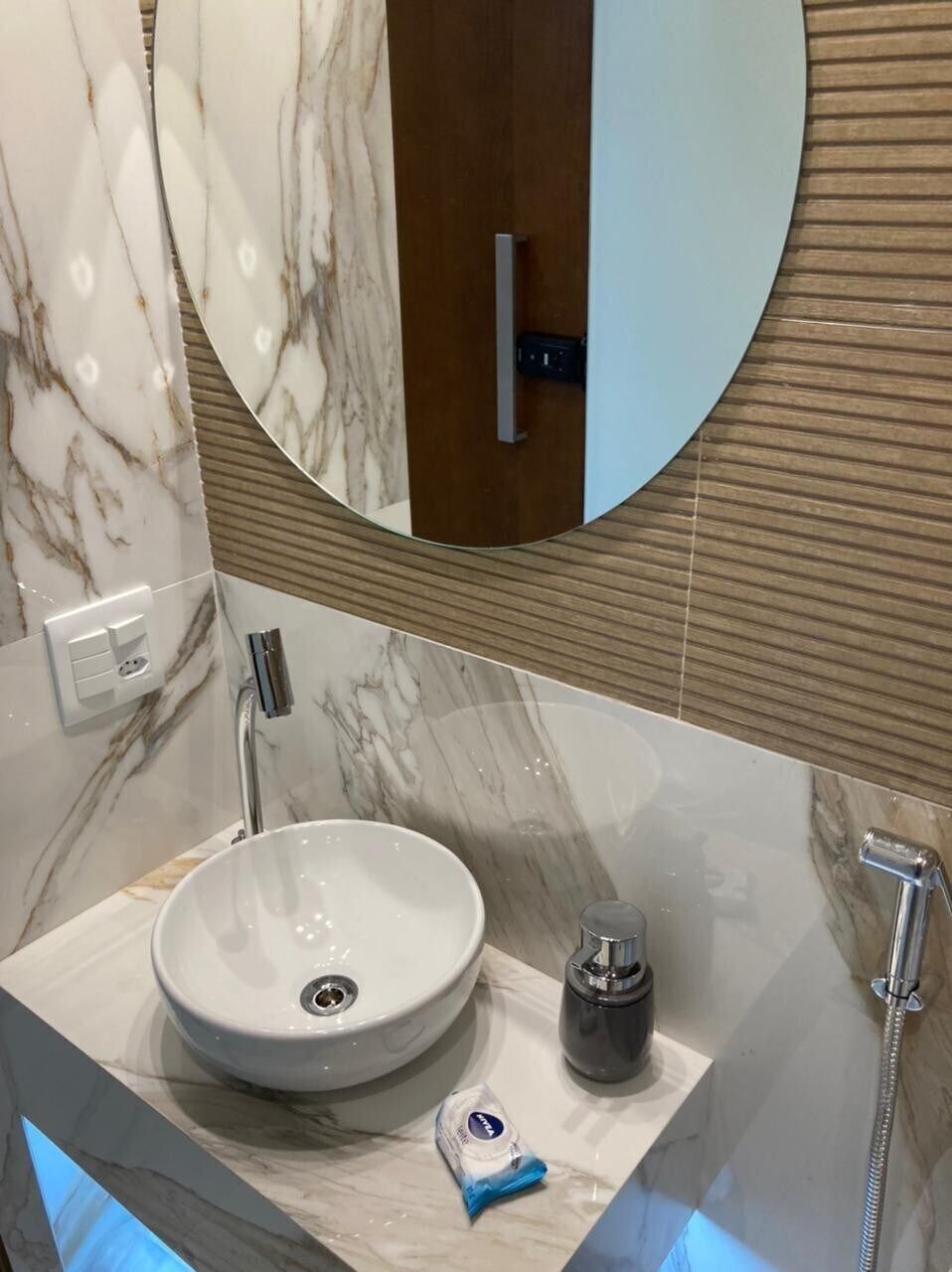 A bathroom with a marble sink, a round mirror, and a handheld showerhead.