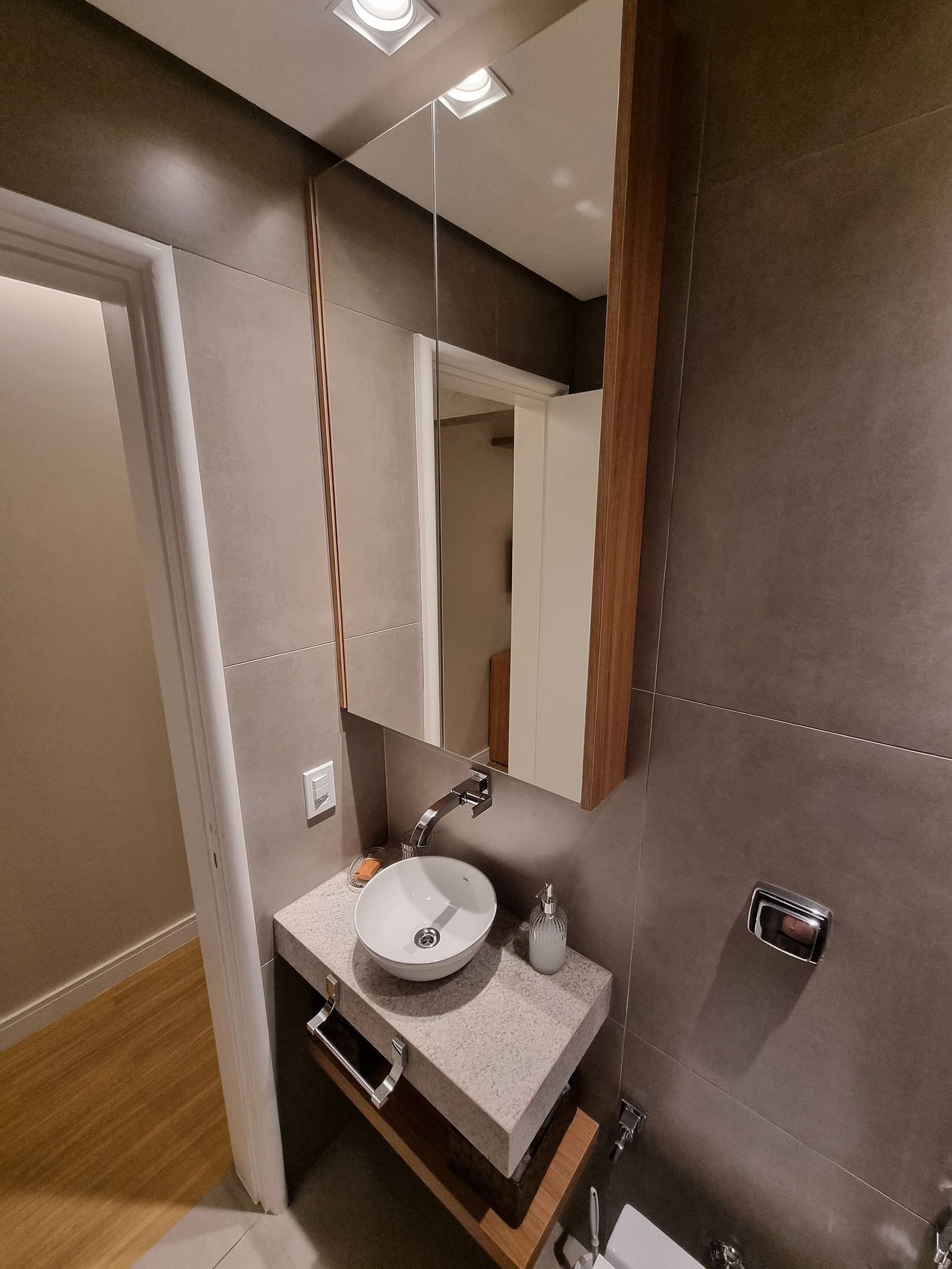 A modern bathroom with a white sink, a mirror, and a wooden vanity.