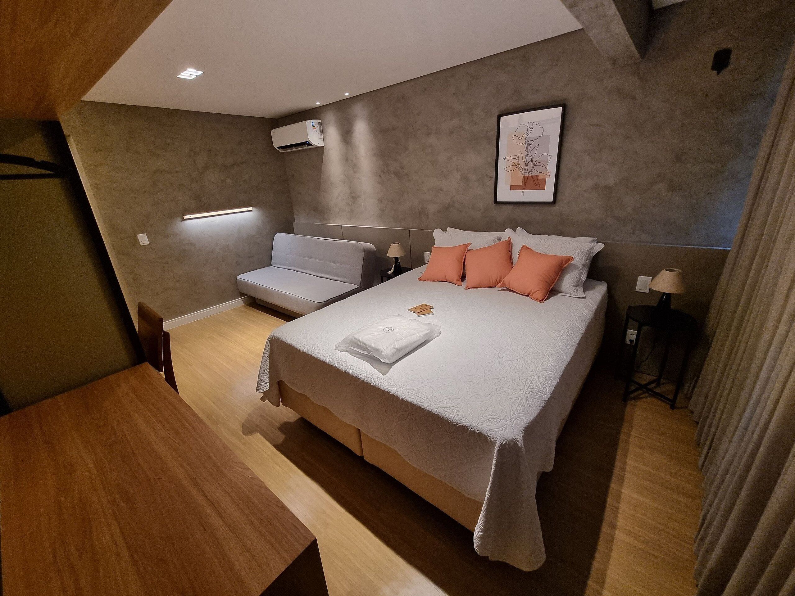 A modern bedroom with a bed, a sofa, a desk, and a wall-mounted air conditioner.