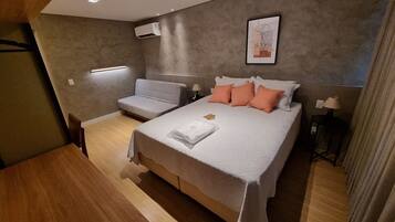 A modern bedroom with a bed, a sofa, a desk, and a wall-mounted air conditioner.