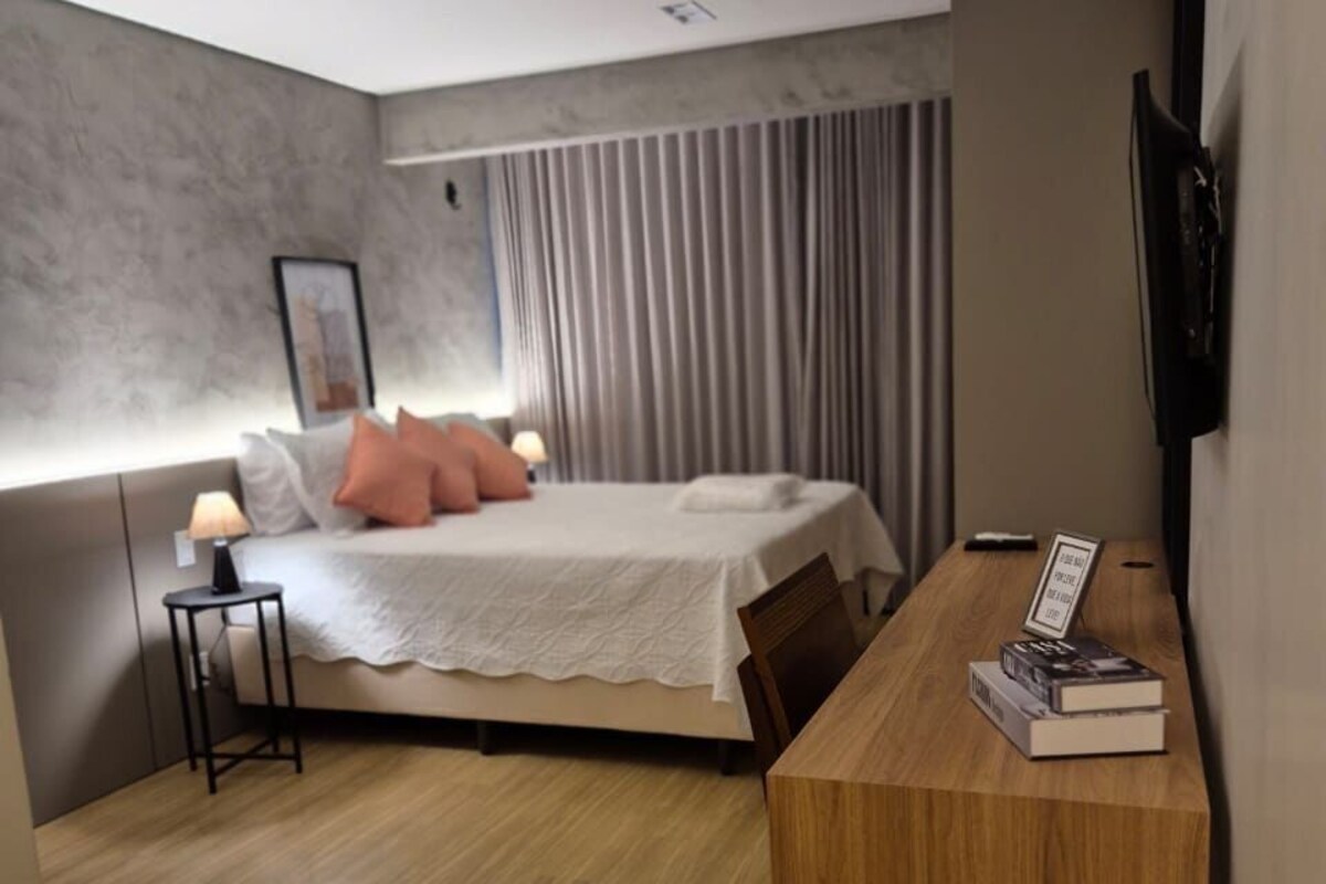 A modern hotel room with a bed, bedside table, and a desk with books.