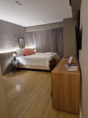 A modern hotel room with a bed, bedside table, and a desk with books.