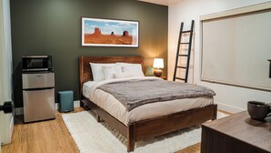 Un dormitorio con cama, mesita de noche, lámpara, microondas y cubo de basura.